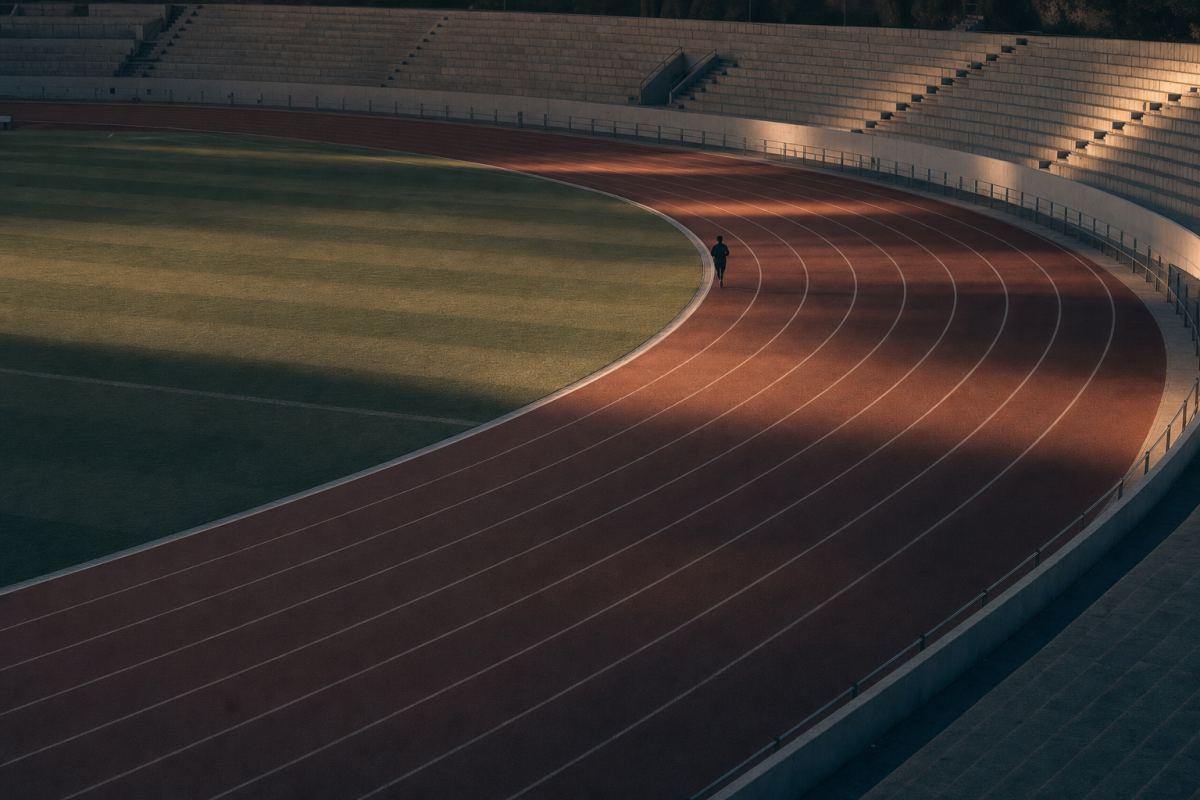 Einzelner Läufer in der Kurve eines leeren Leichtathletikstadions im Morgenlicht
