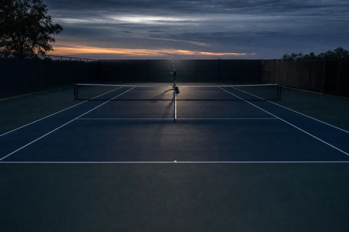 Einzelner Spieler in der Ferne an der Grundlinie eines Tennisplatzes in der Dämmerung