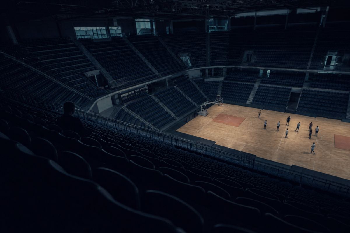 Große Halle vom oberen Rang aus fotografiert, leere dunkle Sitzreihen im Vordergrund, weit unten das beleuchtete Spielfeld