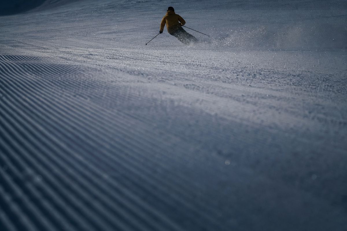 Präparierte Trainingspiste in kaltem Licht, im oberen Bilddrittel ein einzelner Skifahrer von hinten